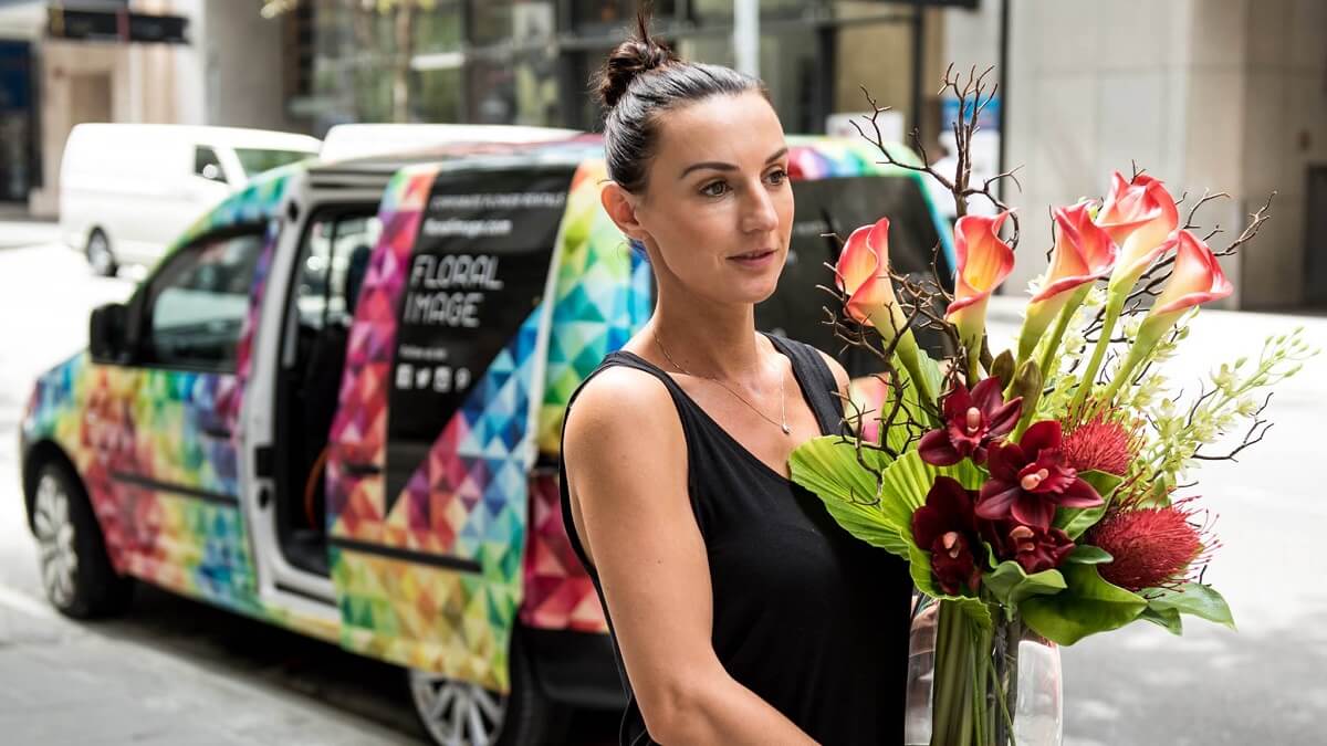 Floral Images Woman Franchisee in front of van holding flowers